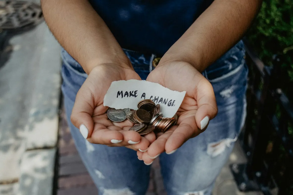 Cupped hands holding coins and a torn note that reads "Make a change"
